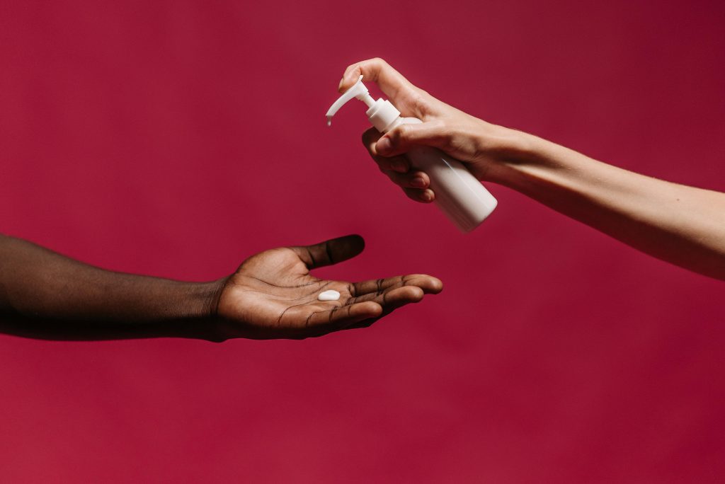 Close-up of hands applying lotion from a pump bottle against a vibrant red background.