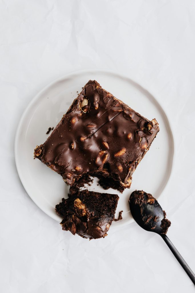 Indulgent chocolate brownie with nuts on a plate and spoon. Perfect dessert.
