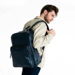 Caucasian man with beard wearing a stylish leather backpack in a studio setting.