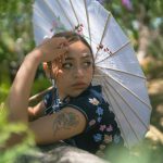 A serene portrait of a woman holding a parasol in a lush garden, showcasing a contemplative expression.