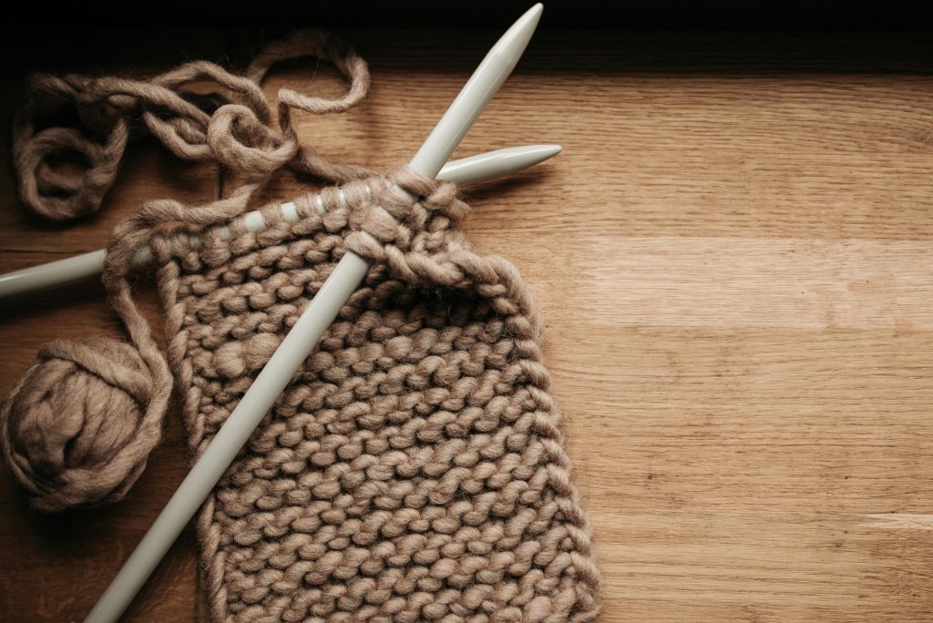 Detailed image of knitting needles, yarn, and a knitting project on a wooden table.