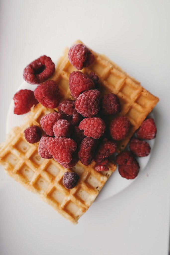 A close-up of golden waffles topped with ripe red raspberries, perfect for a tasty breakfast.