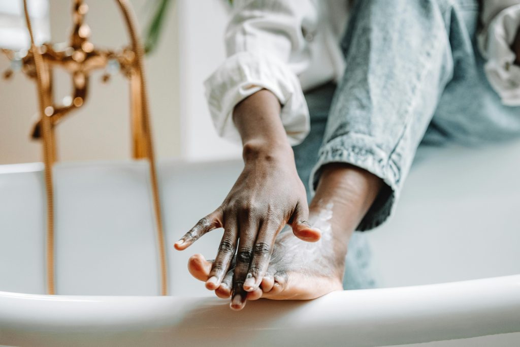 Focused view of a person applying foot cream while sitting on a bathtub edge.
